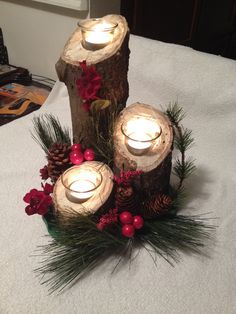 three lit candles are placed on top of some logs with pine cones and red berries