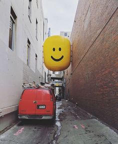 a red van parked next to a tall brick building with a smiley face sign hanging from it's side