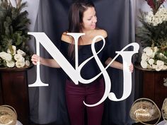 a woman holding up the letter n and j in front of her is surrounded by flowers