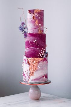 a three tiered cake with purple and gold designs on it's side, sitting on top of a metal stand