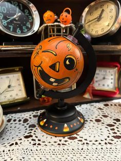 an orange halloween pumpkin on top of a black stand next to clocks and other items