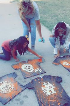 three girls are painting on the ground with orange chalk and scissors in front of them