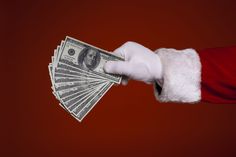 santa claus's hand holding money in front of a red background with white gloves