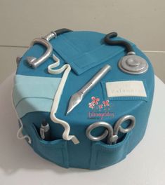 a blue cake with scissors and dental instruments on it's top, sitting on a table