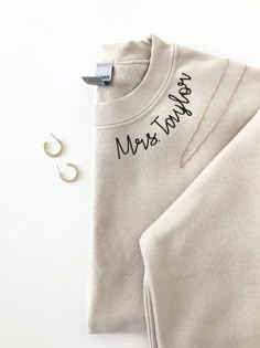 a white shirt with the words mean thank written on it next to two pairs of earrings