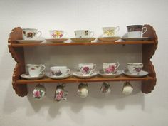 tea cups and saucers are lined up on a wooden shelf in front of a white wall