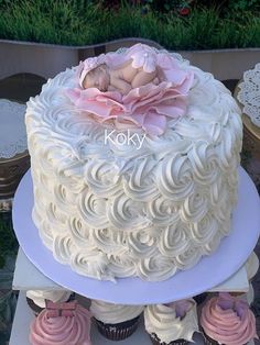 a baby is laying on top of a white cake with pink frosting and cupcakes