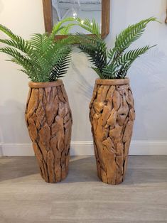 two wooden vases with plants in them sitting on the floor next to a mirror