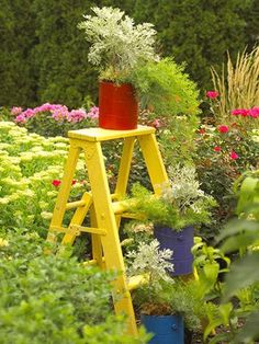 a garden filled with lots of flowers and plants next to a yellow ladder in the middle