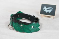 a green leather collar with leaves on it next to a small black square sign that says no dogs allowed