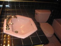 a pink sink sitting next to a toilet in a black tiled bathroom with gold trim