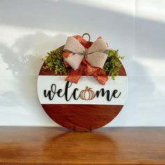 a welcome sign with two wedding rings on it sitting on a wooden table next to a wall