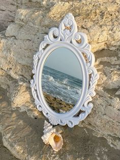 a mirror sitting on top of a rock next to the ocean