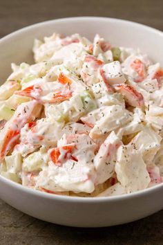 a white bowl filled with coleslaw salad on top of a wooden table next to a fork