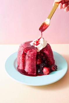 someone is spreading icing onto a cake on a plate with berries and whipped cream