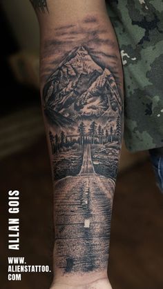 a man's arm with a mountain and road tattoo on the left side of his arm