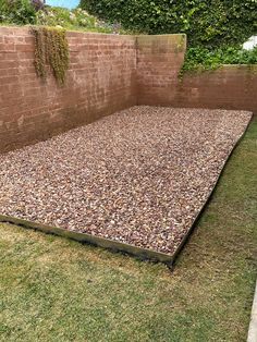 an empty backyard with gravel and grass in the ground, next to a brick wall