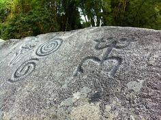 the rock has carvings on it and is surrounded by green trees in the back ground