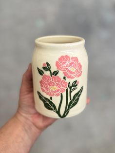 a hand holding a vase with pink flowers painted on the outside and green leaves on the inside