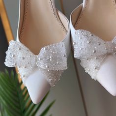 a pair of white shoes with pearls and bows on the toes are sitting next to a plant