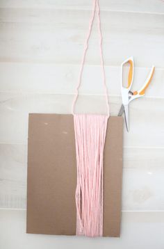 a pair of scissors sitting on top of a piece of cardboard next to some pink yarn