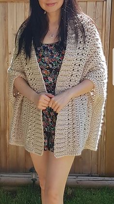 a woman standing in front of a wooden fence wearing a short dress and cardigan