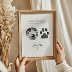 a person holding up a framed photo with dog paw prints on it and a plant in front of them