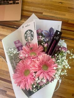 a bouquet of pink flowers sitting on top of a white envelope next to a laptop