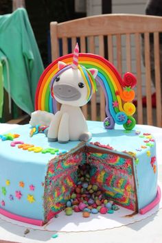 a birthday cake with a unicorn on top and candy in the middle, surrounded by rainbow decorations