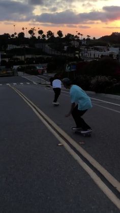 two people on skateboards riding down the street at sunset with palm trees in the background