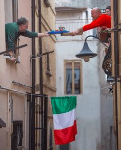 two men are hanging from the side of a building and one is holding an italian flag