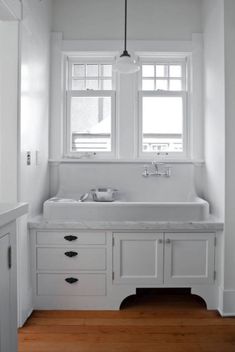 an all white kitchen with wood flooring and large window above the sink is shown