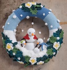 a knitted wreath with snowmen in the middle and daisies around it, hanging on a wall