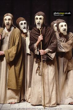 five men in white masks standing next to each other with one holding a cane and the other wearing a mask