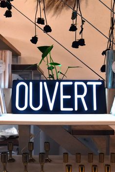 there is a sign that says ouvert hanging from the ceiling above candles and vases