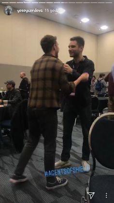 two men are dancing in an auditorium with other people sitting at tables and talking to each other