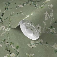 a roll of wallpaper with white flowers on green paper and floral design in the background