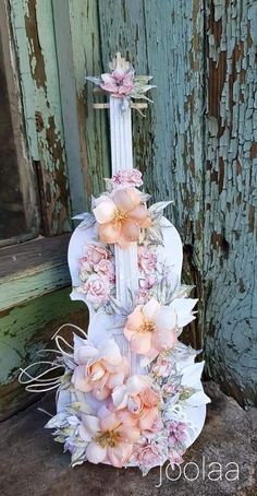 a white guitar decorated with pink flowers on top of a wooden floor next to an old door