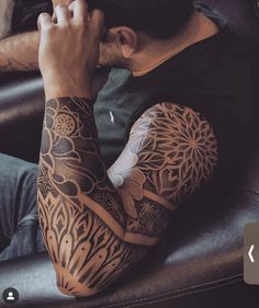 a man sitting on top of a couch with tattoos on his arms and arm sleeves