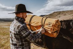 a man wearing a hat and carrying a bag on top of a horse in a field