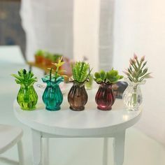 small glass vases with plants in them sitting on a white table next to a window