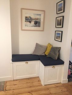 a corner bench with two storage bins underneath it and pictures on the wall above