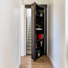 an open bookcase in the corner of a hallway with stairs leading up to it