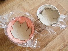 two leaf shaped bowls sitting on top of a wooden table next to plastic wrappers