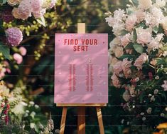 a pink sign sitting on top of a wooden easel in front of some flowers