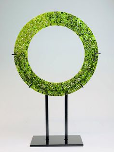 a green circular sculpture sitting on top of a metal stand