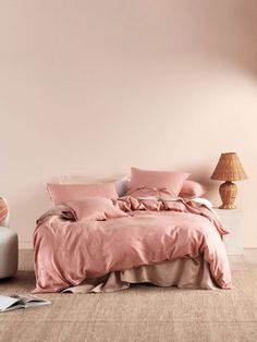 a bed with pink linens and pillows in a neutral bedroom, next to a lamp