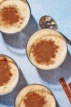 three desserts with cinnamon on top are sitting in small glass bowls next to two spoons