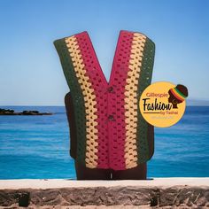 a crocheted vest sitting on top of a stone wall next to the ocean