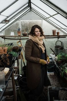 a woman standing in a greenhouse holding a potted plant